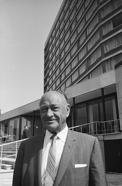 Schwarz-weiß-Foto von Conrad Nicholson Hilton, im Hintergrund ist sein Hotel in Amsterdam zu sehen.