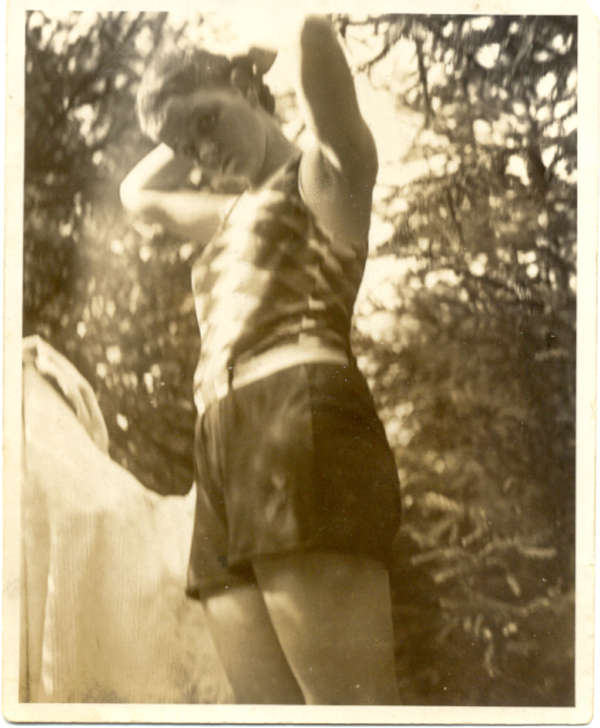 Alte Fotografie einer jungen Frau in sommerlicher Kleidung vor Bäumen.