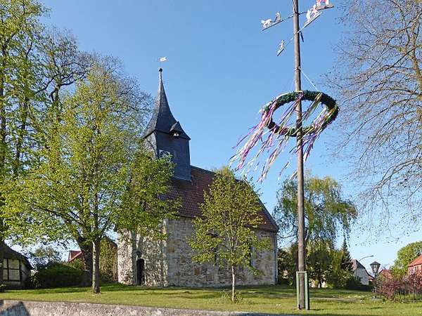 Foto eines Maibaums vor einer alten Kirche.