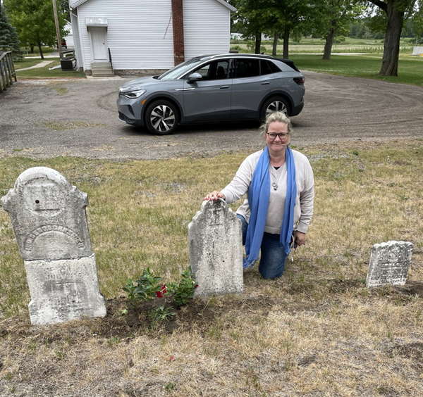 Andrea Bentschneider kniet neben dem Grabstein Ihres Ur-Ur-Ur-Ur-Großvaters auf einem US-amerikanischen Friedhof.