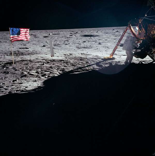 Foto von Neil Armstrong bei Arbeiten auf dem Mond nahe der Mondlandefähre, am Rand die gehisste amerikanische Flagge
